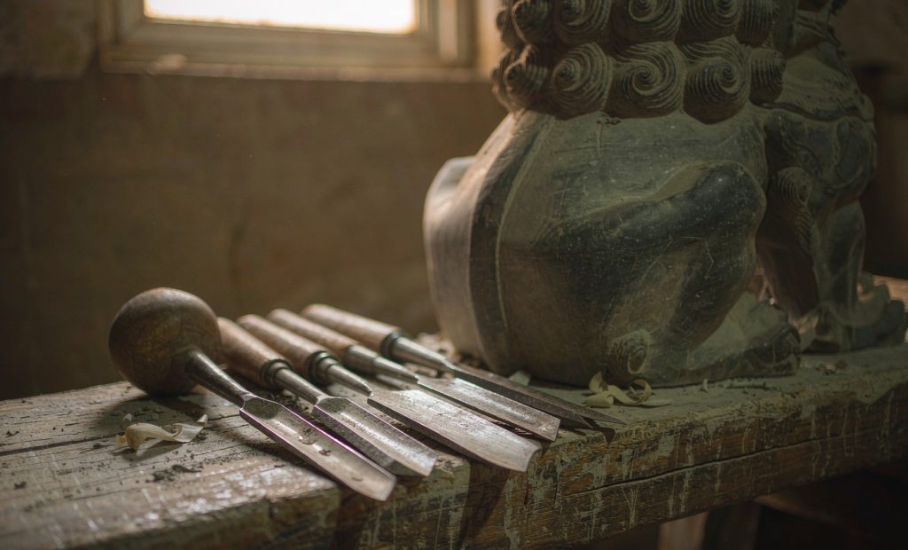 Illustration: chisels and a mallet on a workbench beside a half-finished carved stone lion