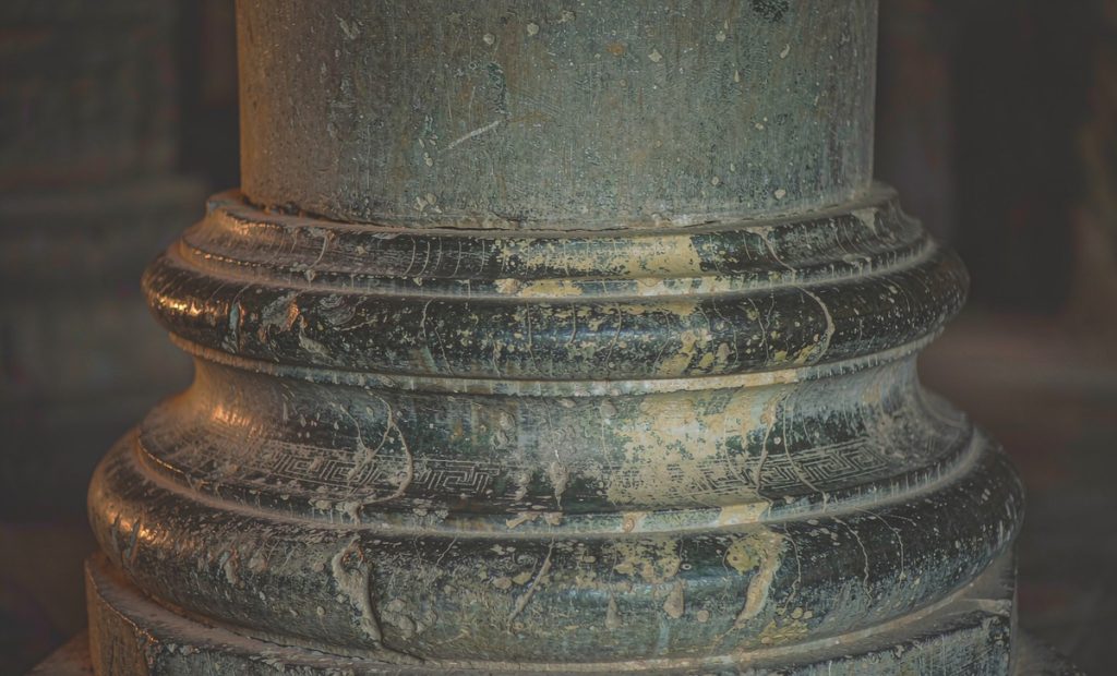 Illustration: the base of an old carved stone column, weathered and pitted