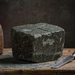 A block of dark green speckled stone on a workshop bench beside a chisel and mallet (illustration)
